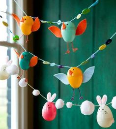 some paper birds and rabbits are hanging from a string in front of a green wall