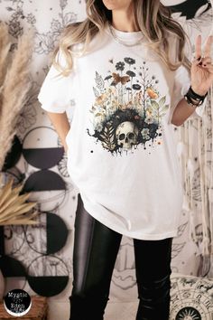 This whimsigoth fashion shirt is perfect for anyone who loves dark cottagecore, goblincore and whimsigoth aesthetics! It features a unique watercolor painting of a skull amongst flowers and butterflies. The perfect combination of whimsical gothic and cozy cottagecore, this tee will have you standing out in any crowd. Show off your fandom with this one-of-a-kind whimsigoth shirt. Whether you're attending a festival, meeting up with friends, or just want to add some color to your wardrobe, this sh Gothic Skull Print T-shirt For Fall, Fairy Grunge Long Sleeve T-shirt For Fall, Fairy Grunge Cotton Tops For Fall, Fall Fairy Grunge Cotton Tops, Cotton Skull Print Shirt For Fall, Gothic Skull Print Tops For Fall, Fall Skull Print Cotton Shirt, Fall Cotton Shirt With Skull Print, Fairy Grunge Short Sleeve T-shirt For Fall