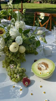 an arrangement of flowers, fruit and greenery is displayed on a table in a park setting