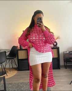 a woman taking a selfie while wearing a pink crochet sweater and white skirt