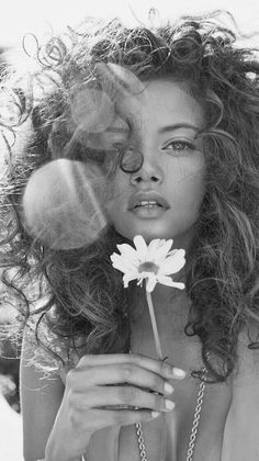 a black and white photo of a woman with long hair holding a flower in front of her face