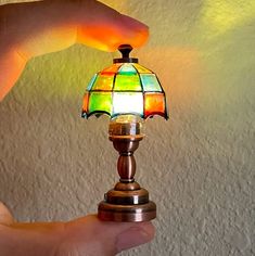 a hand holding a small lamp with a colorful light on it's base,