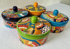 three brightly colored dishes with lids on a white tableclothed surface, one has an orange lid and the other is green