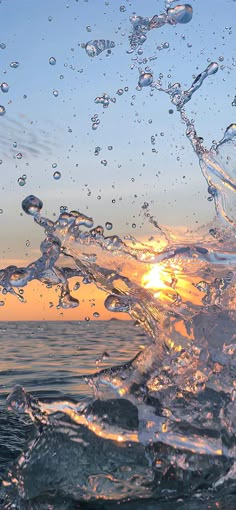 the sun is setting over the ocean with water splashing on it's surface