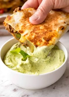 a hand holding a piece of quesadilla over a bowl of guacamole