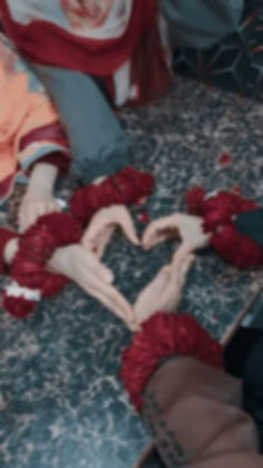 two hands making a heart shape out of yarn on the floor in front of someone's feet