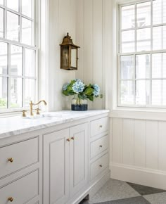 a white kitchen with marble counter tops and gold faucets on the windowsill