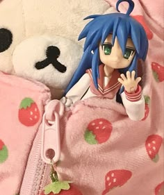 an anime doll is laying in bed next to a stuffed bear and keychain