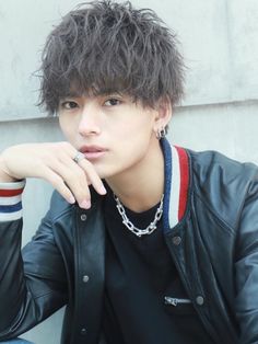 a young man wearing a black leather jacket sitting on a bench with his hand under his chin