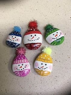 four snowmen painted on rocks with hats and scarves around their necks, sitting on a counter top