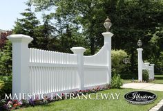 a white picket fence in the middle of a lawn with flowers and trees around it