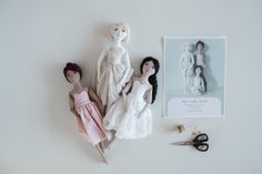 three dolls are sitting on the table next to some scissors and other crafting supplies