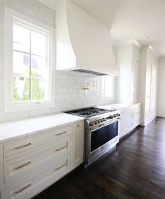 an empty kitchen with white cabinets and wood flooring is pictured in this image, there are two windows above the stove