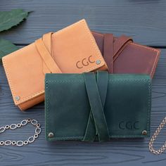 four leather wallets tied together on a wooden table with leaves and chain around them