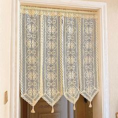 an open window with white lace curtains and tassels hanging from the top, in front of a door