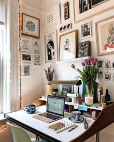 a laptop computer sitting on top of a white desk next to a vase filled with flowers