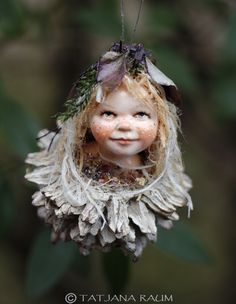 a close up of a doll hanging from a tree with leaves on it's head