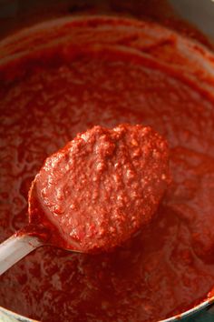 a ladle full of red sauce with a wooden spoon