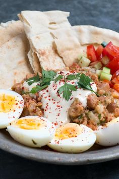 a plate with eggs, tomatoes, cucumbers and pita bread