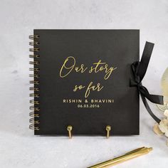 a black and gold wedding guest book next to a pen