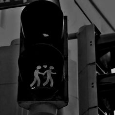 a black and white photo of a traffic light with two people walking on the crosswalk