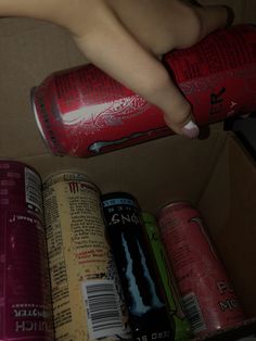 a person reaching for a can of soda in a cardboard box with other cans behind it