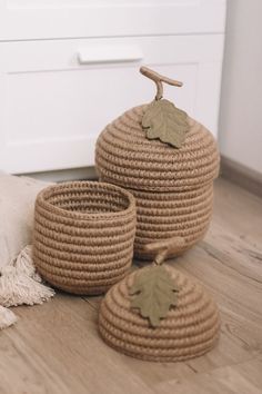 three woven baskets with leaves on them sitting on the floor next to a rug and pillow