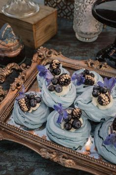 cupcakes with blue frosting and berries on top are sitting in a tray