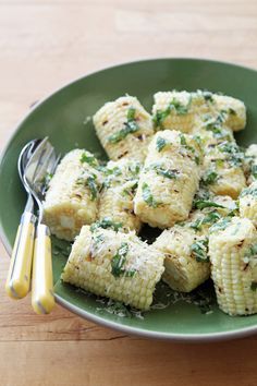 a green plate topped with corn covered in parmesan cheese and herbs next to a fork