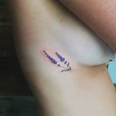 a small tattoo on the side of a woman's stomach with purple flowers and leaves