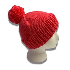 a red knitted hat with a pom - pom on the front and side