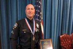 a man in uniform standing next to a plaque with an american flag behind him and a blue curtain