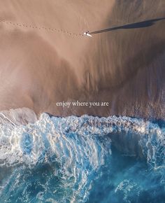 an aerial view of the ocean and sand with a message written on it that says, enjoy where you are