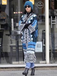 a woman is walking down the street wearing a blue hat and black coat with geometric patterns