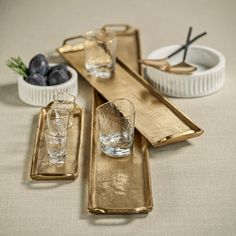 gold serving trays with glasses and olives on the table next to each other