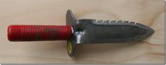 a knife that is on top of a piece of wood with a red tube attached to it