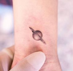 a small saturn tattoo on the wrist