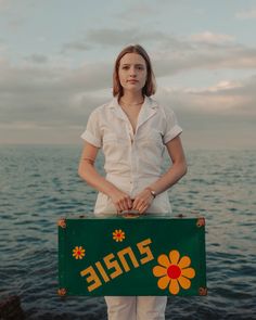 a woman holding a sign that says zniee by the water's edge