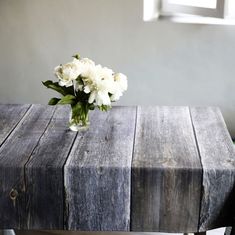 a vase with white flowers sitting on top of a wooden table next to a window