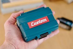 a person holding a blue case with the word custom on it in their left hand