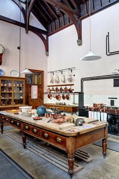 an old wooden table in a room with many items on the tables and hanging lights above it