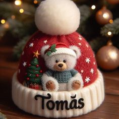 a knitted hat with a teddy bear on it and the word tomas written in black