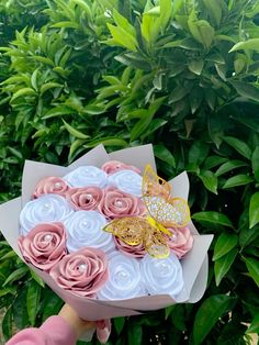 a hand holding a bouquet of pink and white roses with a butterfly on it's top