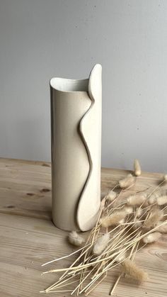 a white vase sitting on top of a wooden table next to dry grass and flowers