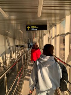 two people walking down an escalator with luggage in their hands and one person wearing a red jacket