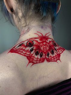 a woman with blue hair has a red butterfly tattoo on her back neck and chest