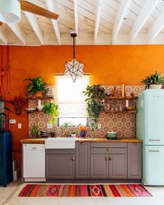 a kitchen with an orange wall and wooden ceiling, white appliances and potted plants