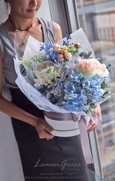 a woman holding a bouquet of blue and white flowers in front of a large window