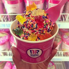 a person holding up a pink cup filled with sprinkles and jelly bears