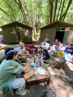 a group of people sitting around a picnic table in the woods with drinks on it